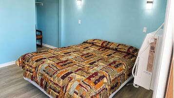 A bedroom with a patterned bedspread, a chair, a bedside table, and a wall-mounted light fixture.