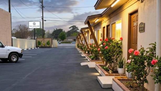 Une rangée de chambres de motel, avec une enseigne indiquant « The Oaks Inn », et une voiture blanche garée sur le parking.