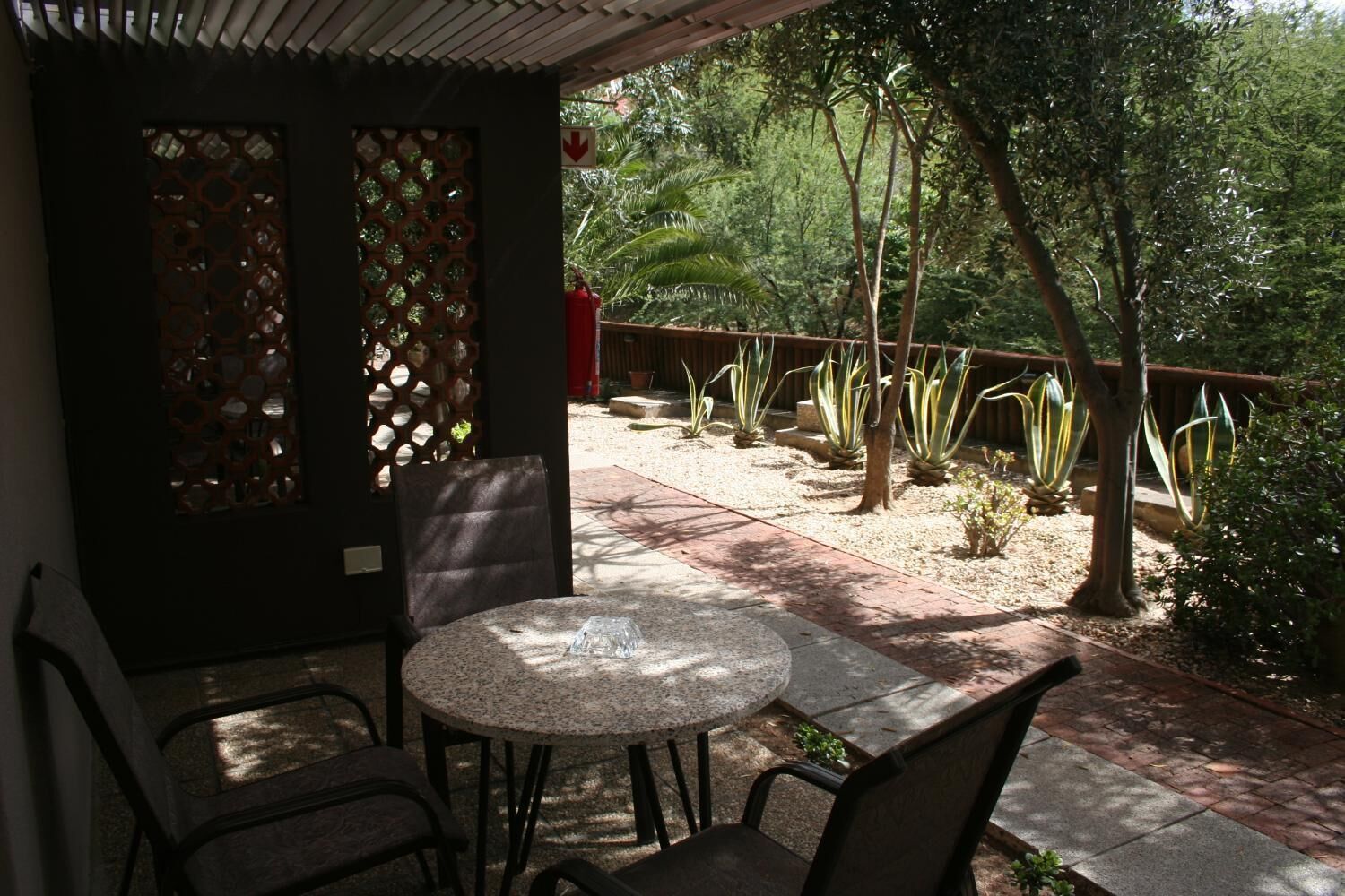 A patio with a round table and chairs, surrounded by a garden with various plants and a wooden fence.
