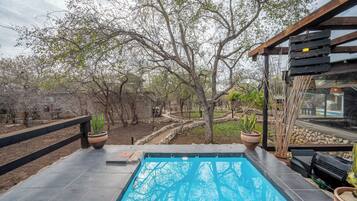 Una piscina con cubierta de madera, rodeada de árboles y plantas en macetas.