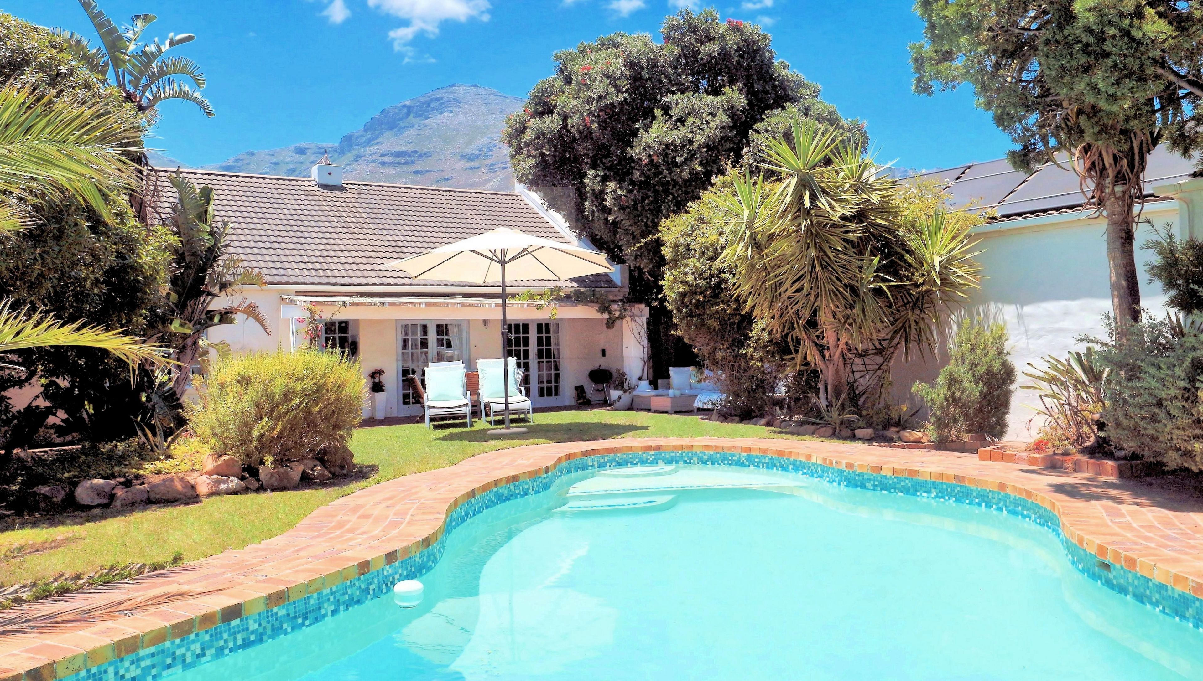 A backyard with a swimming pool, a covered patio, and a mountain in the background.