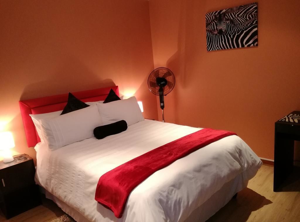 En snyggt bäddad säng med vita och röda sängkläder, en golvfläkt och en väggdekoration med zebrasträck.