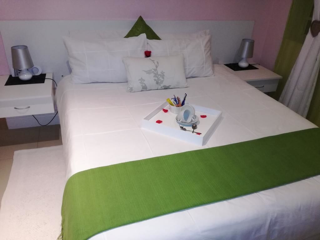 A neatly made bed with a green bedspread, white pillows, and a bedside table with a lamp and a cup.