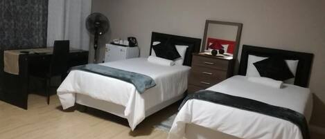 Quarto de hotel com duas camas, uma escrivaninha, uma televisão e uma cômoda.