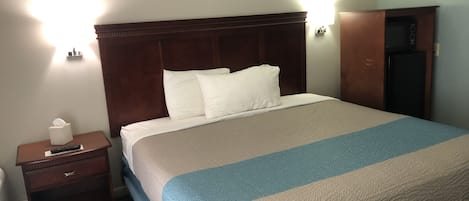 A hotel room with a large bed, a nightstand with a tissue box and remote, and a wooden headboard.