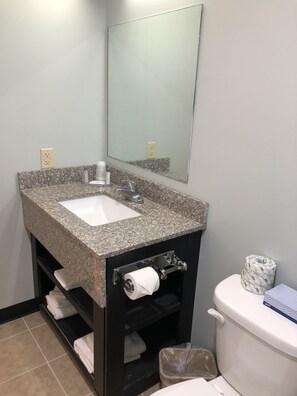 A bathroom with a granite countertop sink, a mirror, a toilet, and a trash bin. - Motel 6 Shartlesville, PA (Bernville)