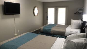 Habitación de hotel con dos camas, un televisor montado en la pared, un espejo redondo y una ventana con persianas.
