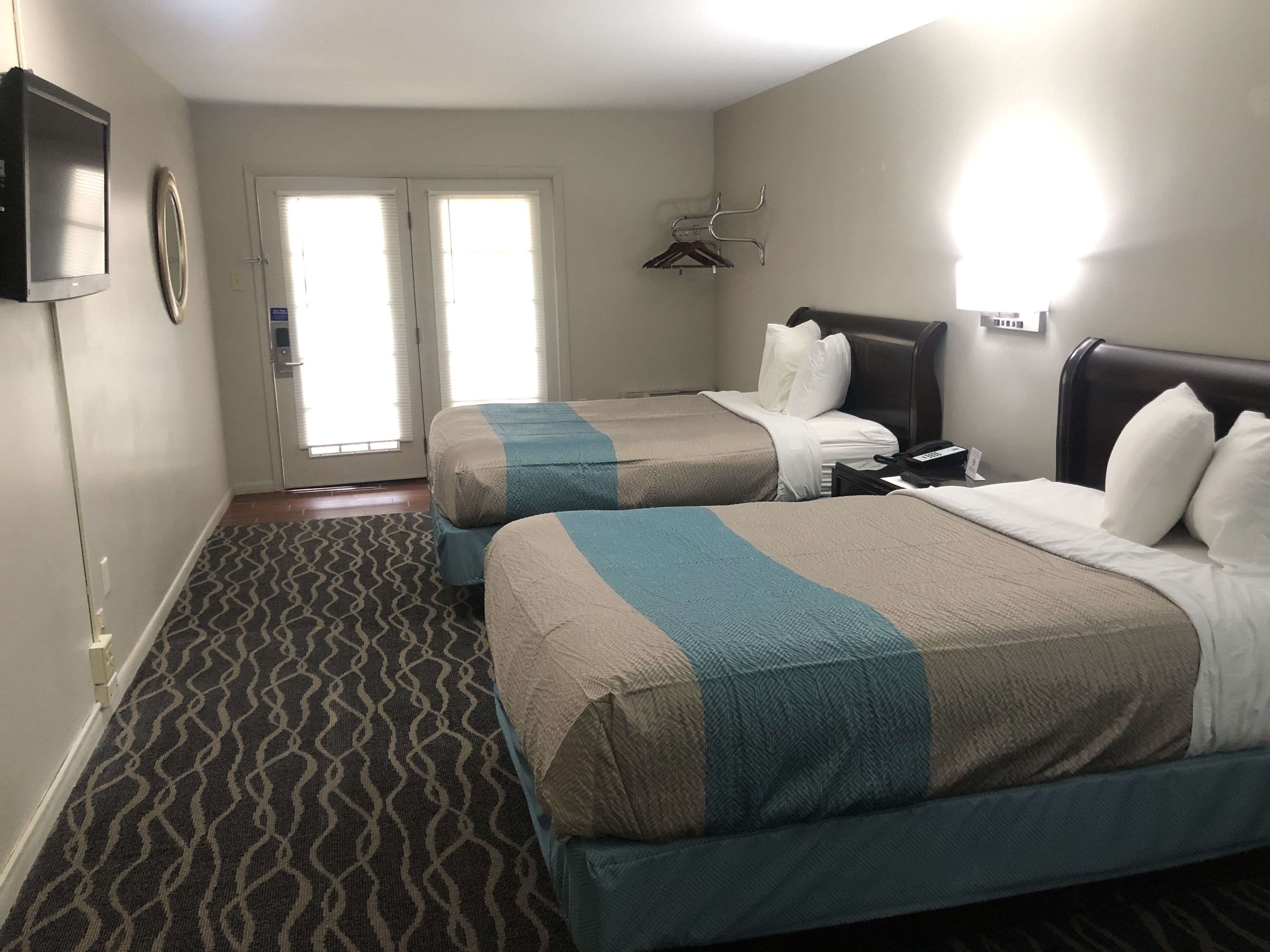 A hotel room with two beds, a television, a door with a view, and a patterned carpet.
