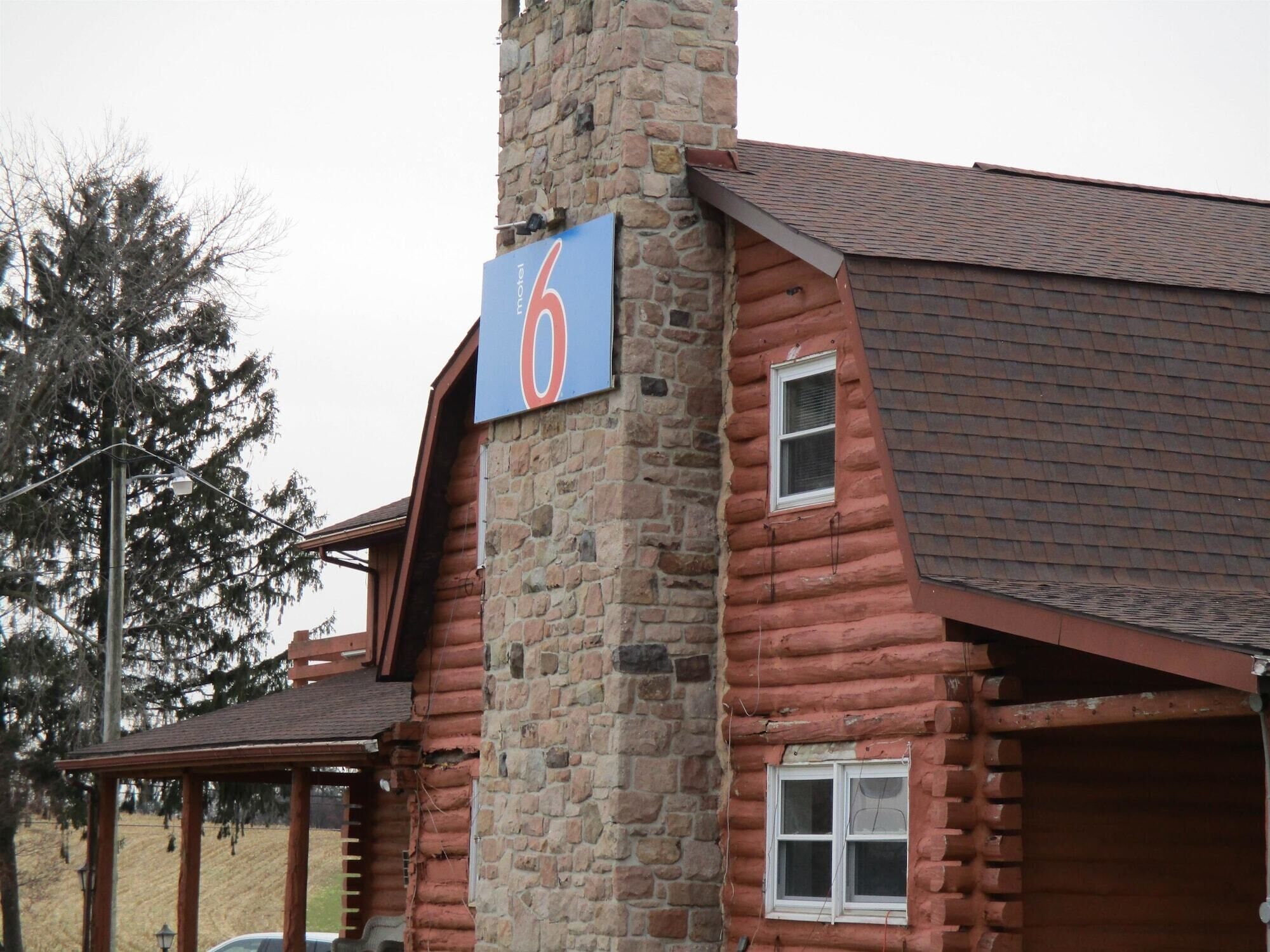 A rustic log cabin with a stone chimney, a porch, and a sign indicating it is number 6.
