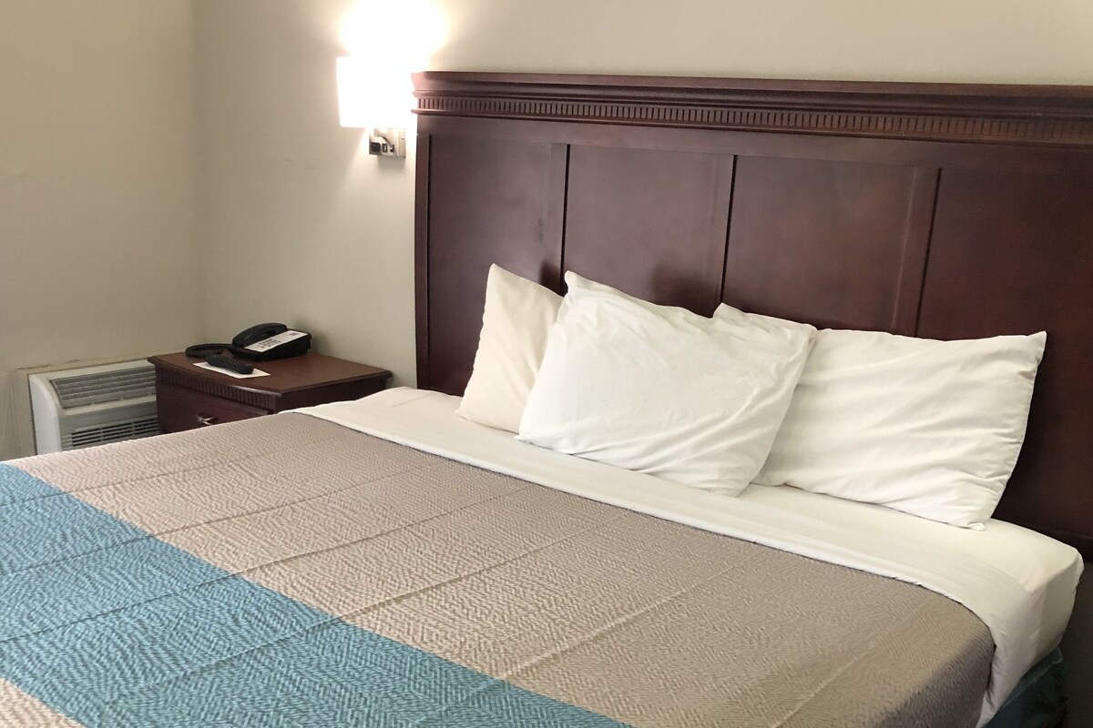 Habitación de hotel con una cama grande, cabecera de madera, mesita de noche con teléfono e iluminación en la pared.