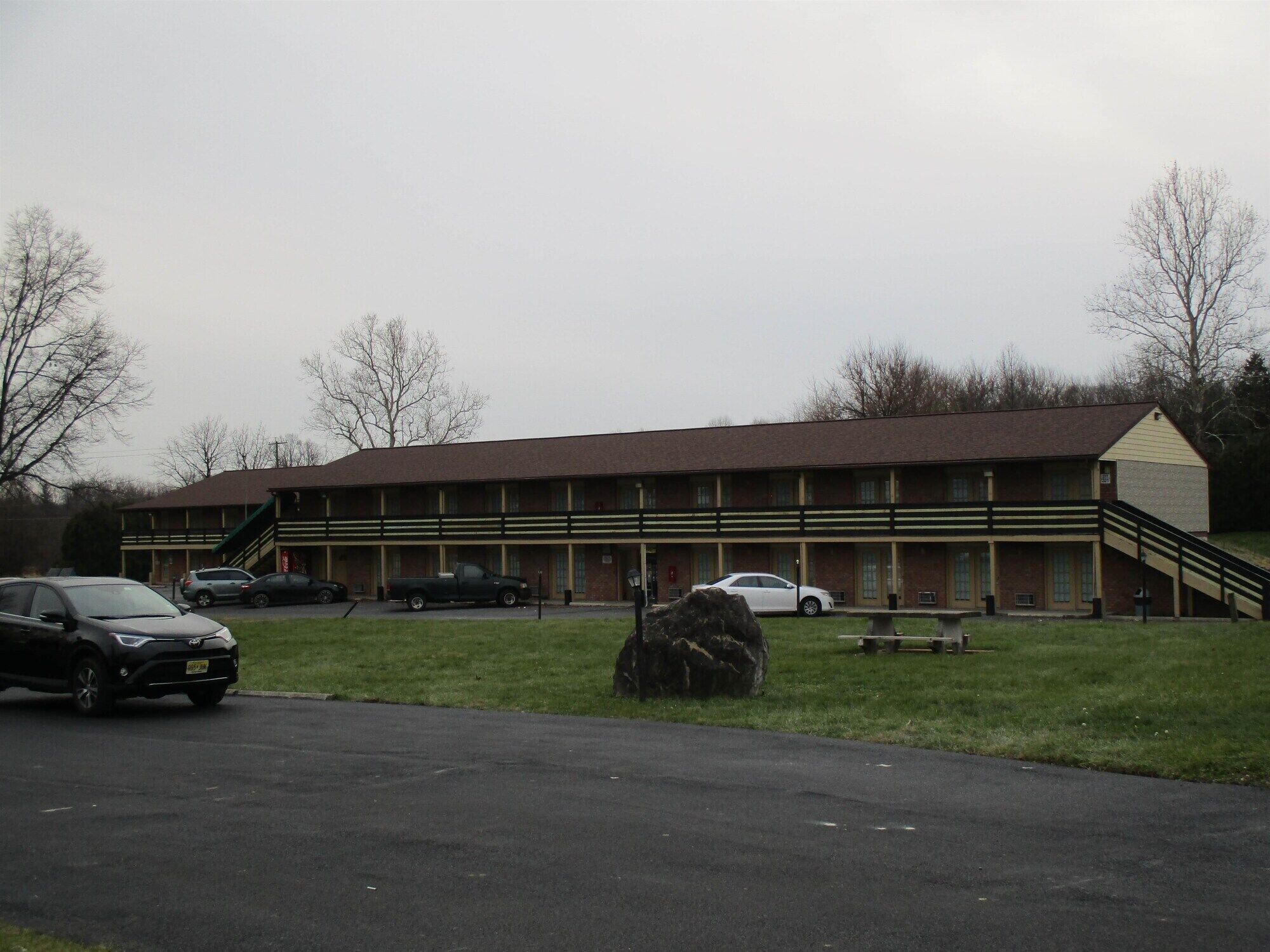 Un motel con fachada de ladrillo, una escalera central y un estacionamiento con varios coches.
