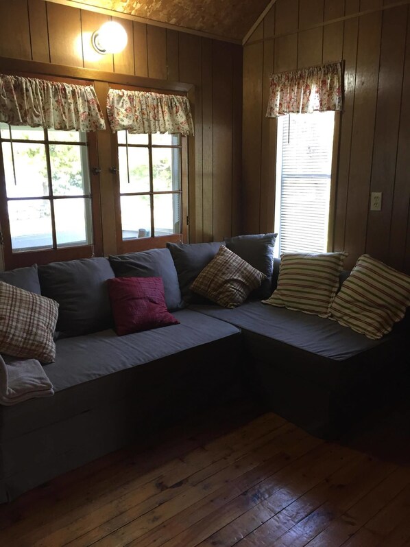 A cozy room with a built-in bench seating area, wooden walls, and large windows with floral curtains. - Maple Grove Cottages (Central Manitoulin)