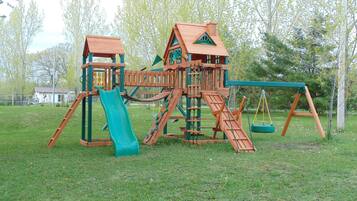 Kids can play on the slide, climb the wall, and swing in this outdoor play area surrounded by trees.