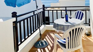 A balcony with a table and chairs, a blue umbrella, and a view of the sea.