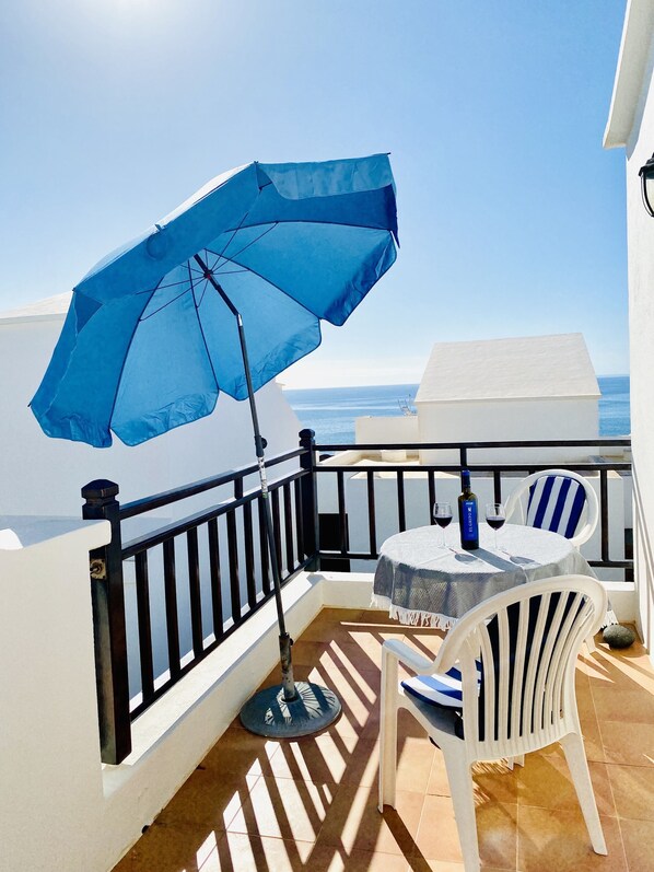 A balcony with a table and chairs, a blue umbrella, and a view of the sea. - Dlx - Bungalow. Fantastic private complex directly by the sea pool, fiber optic internet (Playa Honda)