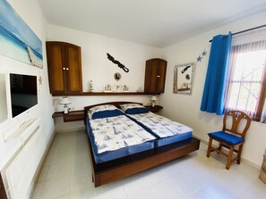A bedroom with a bed, wooden cabinets, a TV, a chair, and a window with curtains. - Dlx - Bungalow. Fantastic private complex directly by the sea pool, fiber optic internet (Playa Honda)