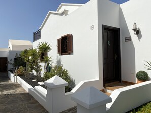 A white building with a black door, a small window with wooden shutters, and a potted plant near the entrance. - Dlx - Bungalow. Fantastic private complex directly by the sea pool, fiber optic internet (Playa Honda)