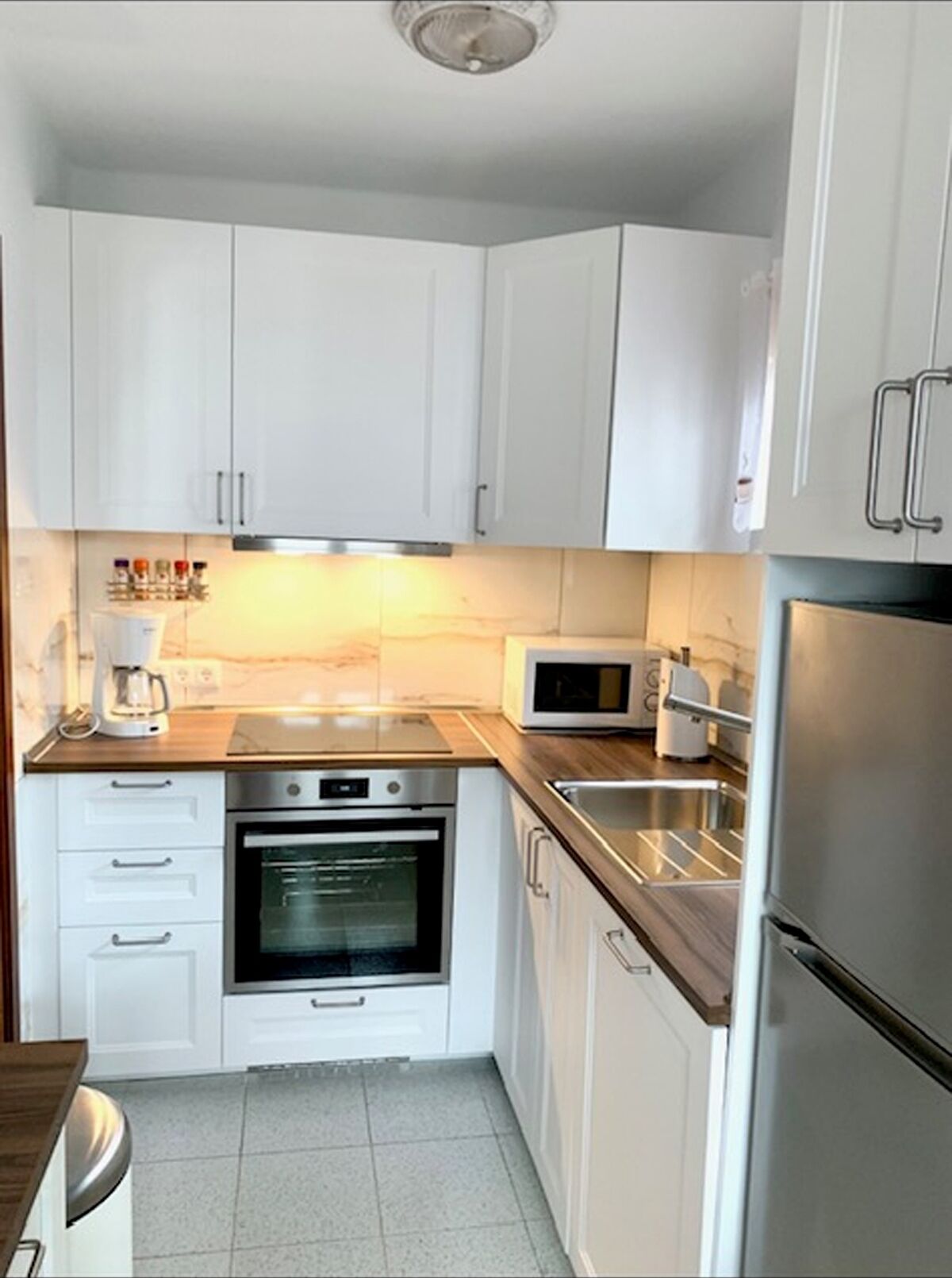 A compact kitchen with white cabinets, a built-in oven, a microwave, and a stainless steel refrigerator.