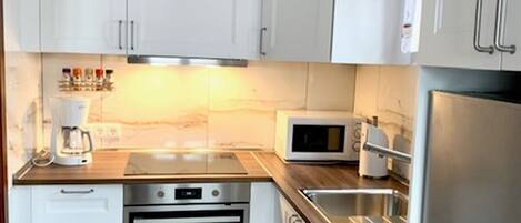A compact kitchen with white cabinets, a built-in oven, a microwave, and a stainless steel refrigerator.