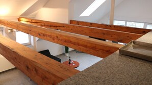 Un intérieur moderne avec des poutres apparentes, une petite table ronde sur laquelle se trouve une bouteille, et une vue sur une plante à travers une fenêtre.