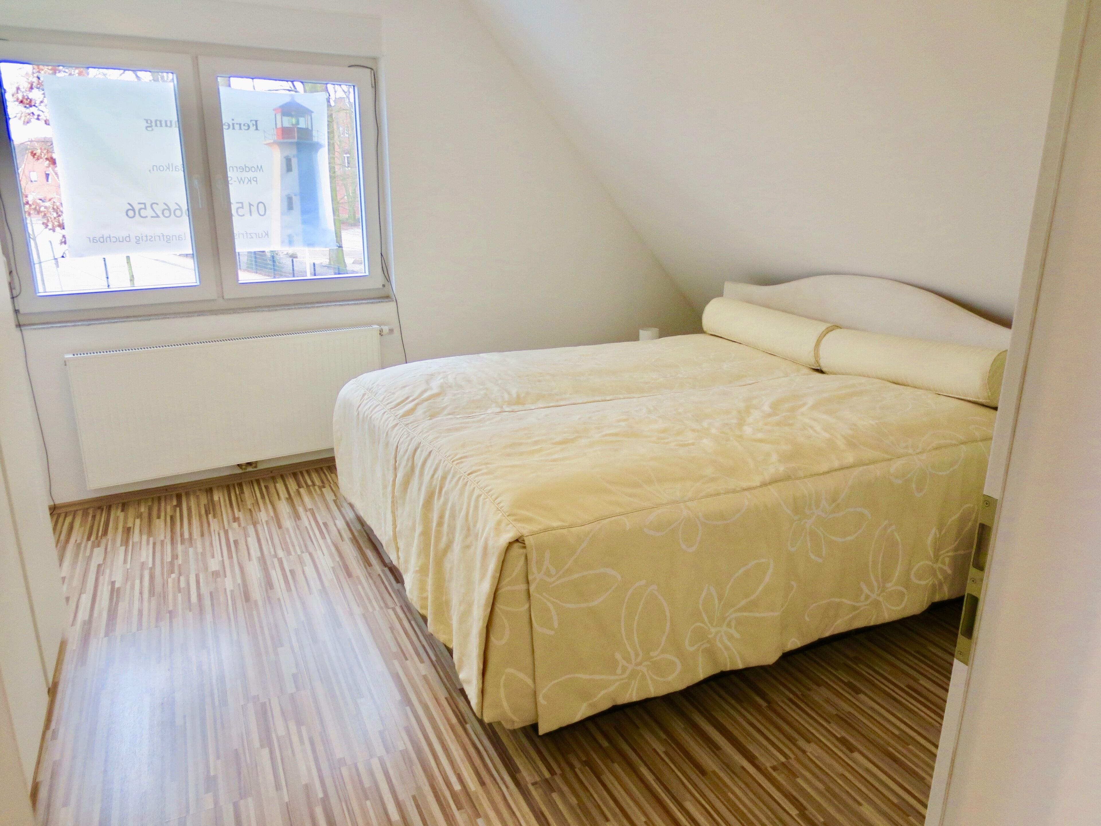 A small, single-bed room with a sloped ceiling, a window with blinds, and a radiator.