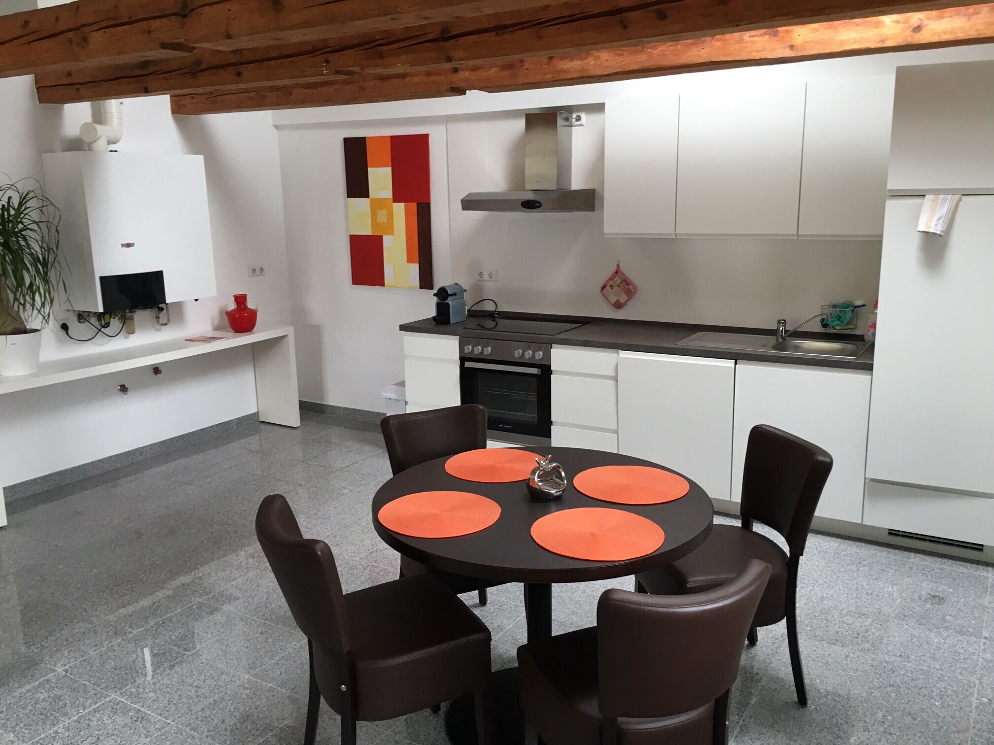 A modern kitchen with white cabinets, a black countertop, and a round table with orange placemats.