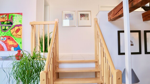 Un escalier avec des rampes en bois menant à un palier. Des tableaux encadrés sont accrochés au mur au-dessus de l’escalier.