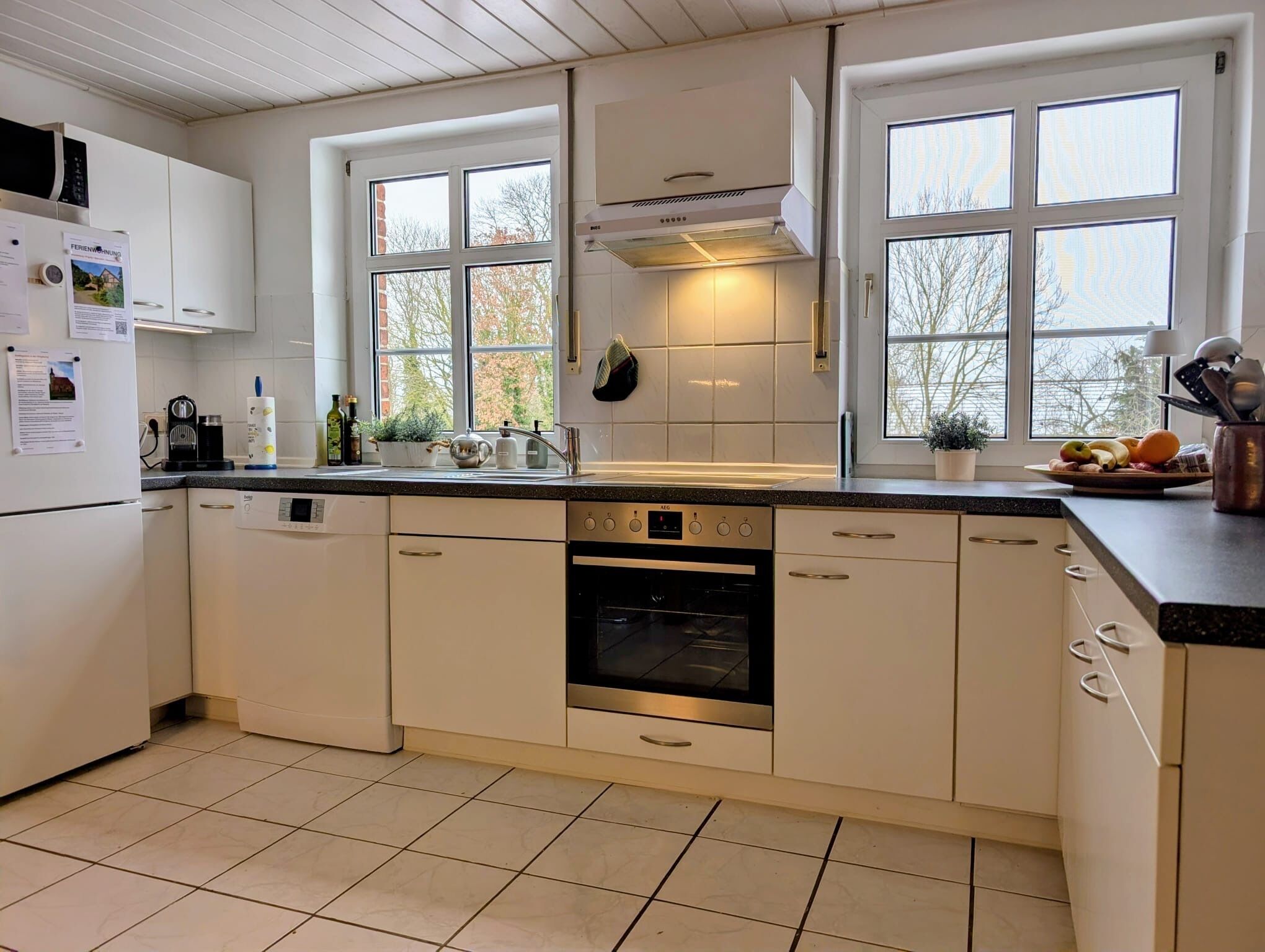 A modern kitchen with white cabinets, a built-in oven, a dishwasher, and a window with a view of trees.