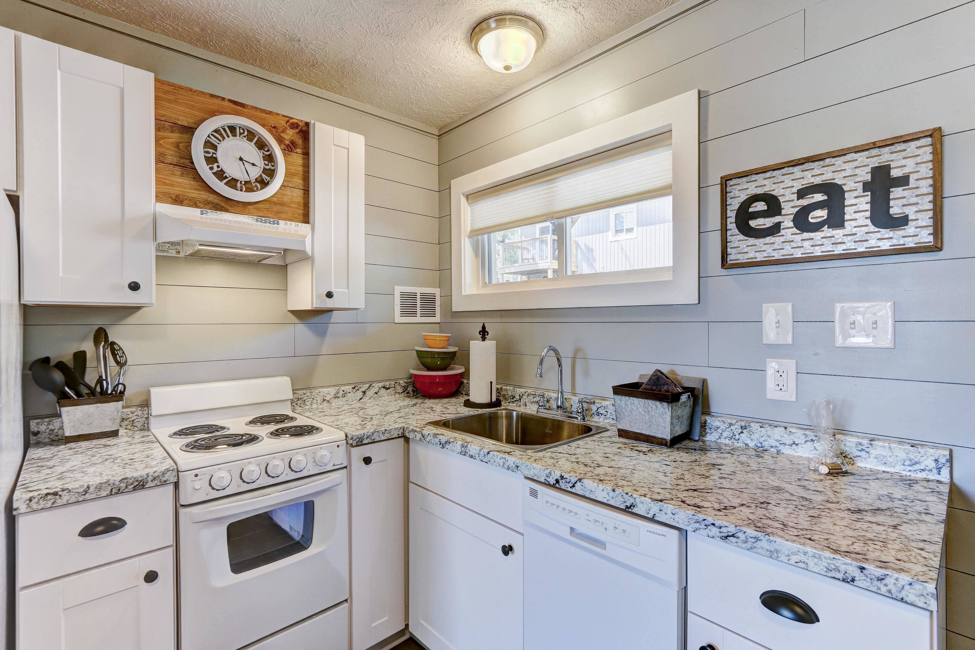 A kitchen with white cabinets, a granite countertop, a stove, a sink, and a window with blinds.