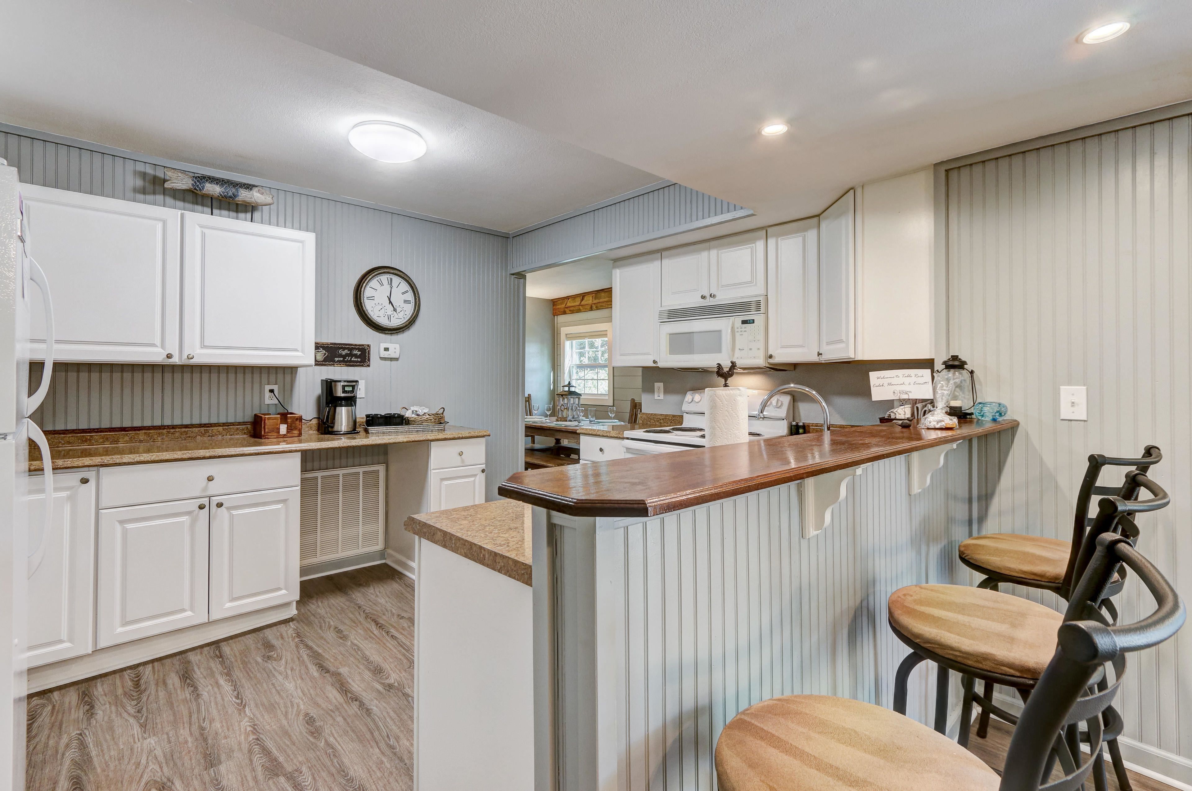 A kitchen with white cabinets, a wooden countertop, a clock, and a microwave.
