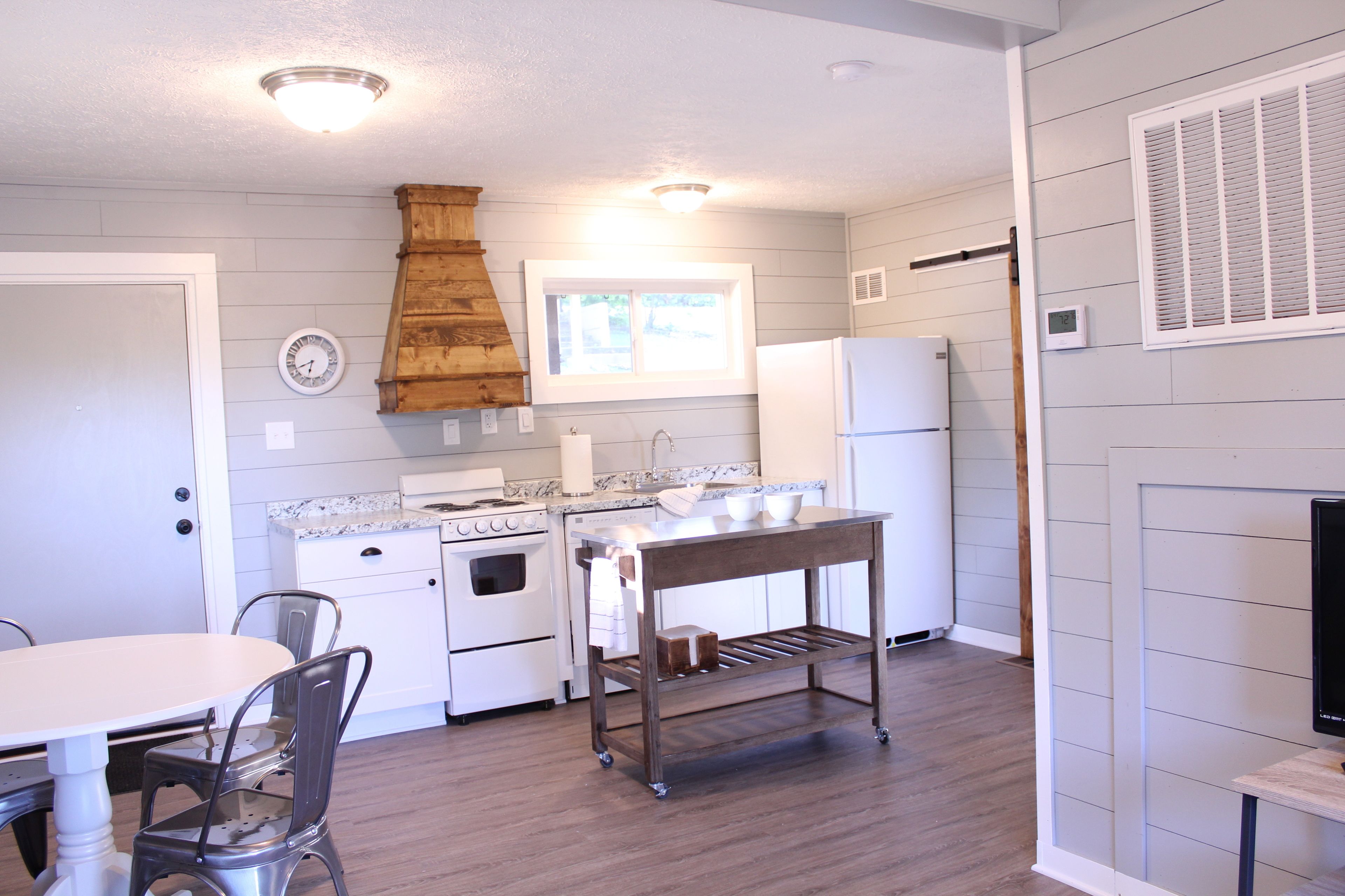 A kitchen with a white stove, oven, and refrigerator, a wooden table, and a window with blinds.