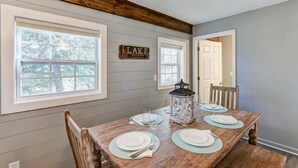 A dining room with a wooden table set for four, large windows, and a 'LAKE' sign on the wall. - Cottages at Fair Haven Cove (Cape Fair)
