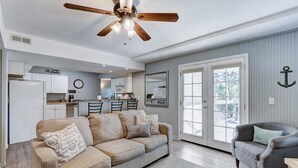 A spacious living room with a beige sofa, a gray armchair, and a ceiling fan. - Cottages at Fair Haven Cove (Cape Fair)