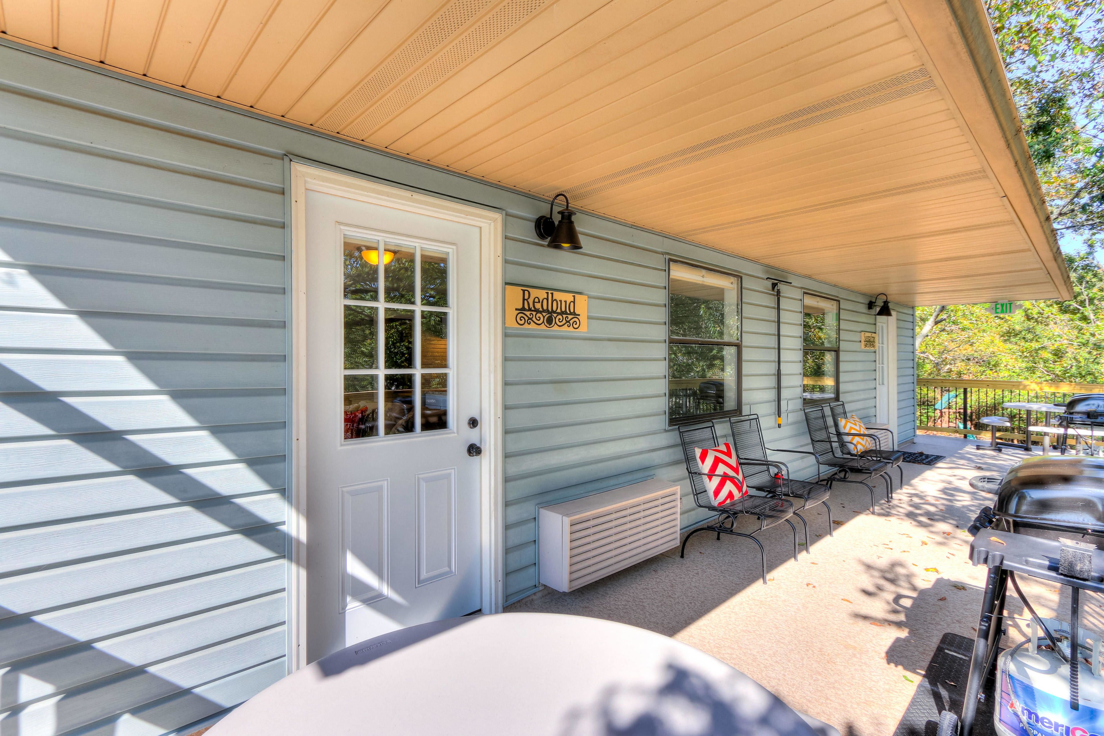 A covered porch with a sign reading "Redbud," outdoor seating, and a grill.
