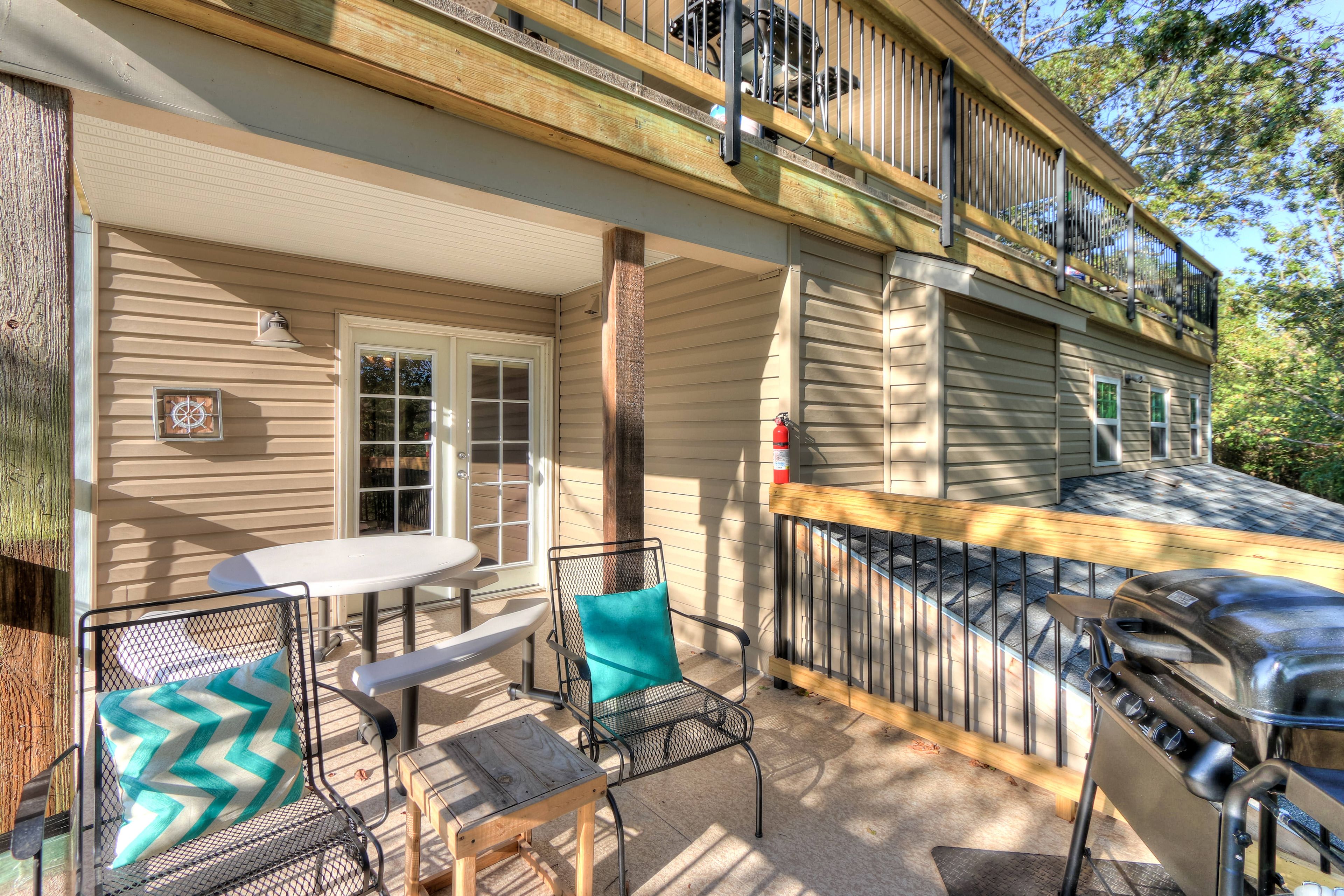 A covered patio with a table and chairs, a grill, and a wooden deck.