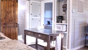 A kitchen with a wooden door, white cabinets, a countertop, and a hanging sign. - Cottages at Fair Haven Cove (Cape Fair)