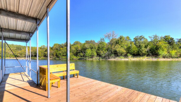 A wooden dock with a bench and a covered area, overlooking a calm lake with trees in the background. - Cottages at Fair Haven Cove (Cape Fair)