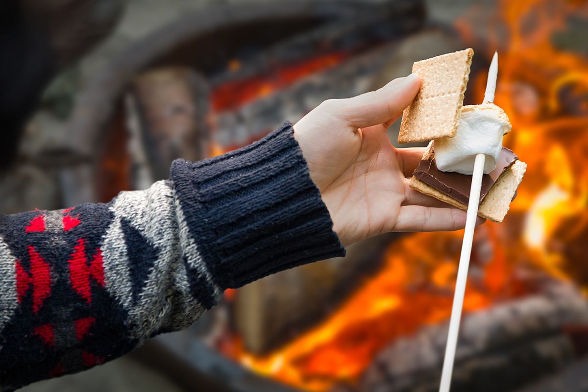Eine Hand hält einen Marshmallow am Spieß über einem Lagerfeuer.