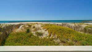 Una playa con una valla de madera, dunas arenosas y un cielo azul despejado.