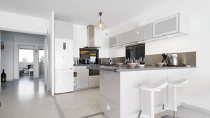 Una cocina moderna con armarios blancos, una isla central con taburetes y una lámpara colgante.
