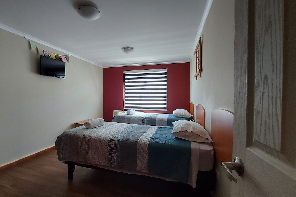 A bedroom with two beds, a television on the wall, and a window with blinds.