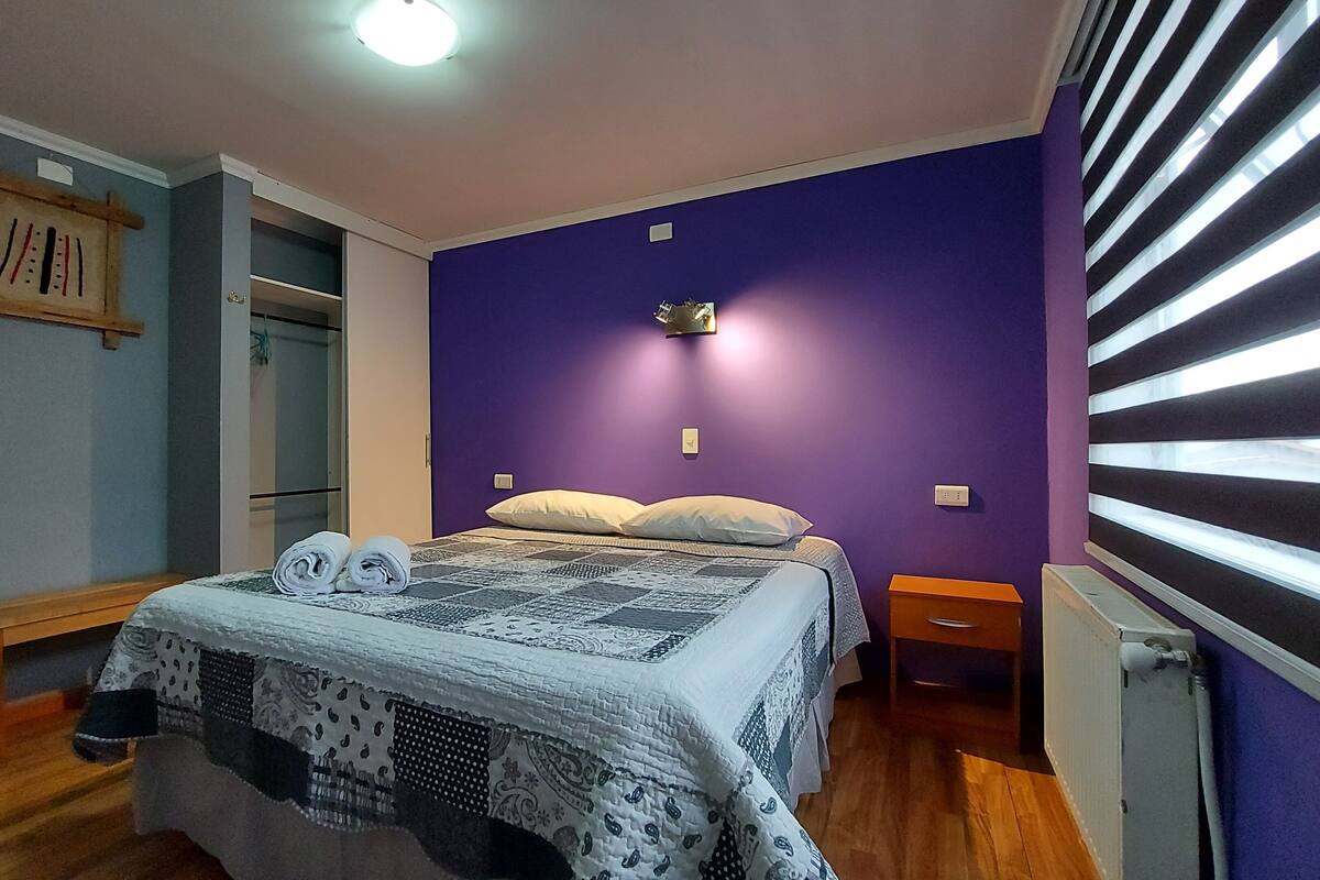 A bedroom with a bed, two bedside tables, a nightstand, a wardrobe, and a radiator.