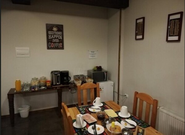 Uma área de refeições com uma mesa posta para dois, uma cafeteira e um micro-ondas em um balcão pequeno.