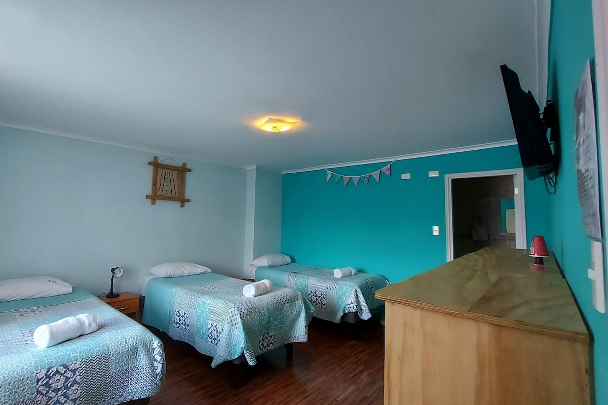A room with two beds, a wooden desk, a wall clock, and a ceiling light.