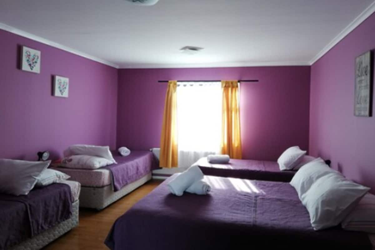 A room with purple walls, two beds, and a window with curtains.