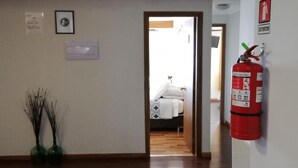Un couloir doté d’un plancher en bois, d’un extincteur fixé au mur et d’une porte donnant sur une chambre.