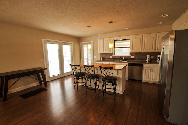 A kitchen with a wooden dining table, four chairs, a refrigerator, and white cabinets. - Beaver Lake Retreat near Rogers, Arkansas (Rogers)