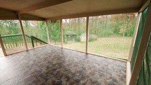 Un patio cubierto con suelo de piedra, ventanas amplias y vistas a un jardín con un cobertizo pequeño.
