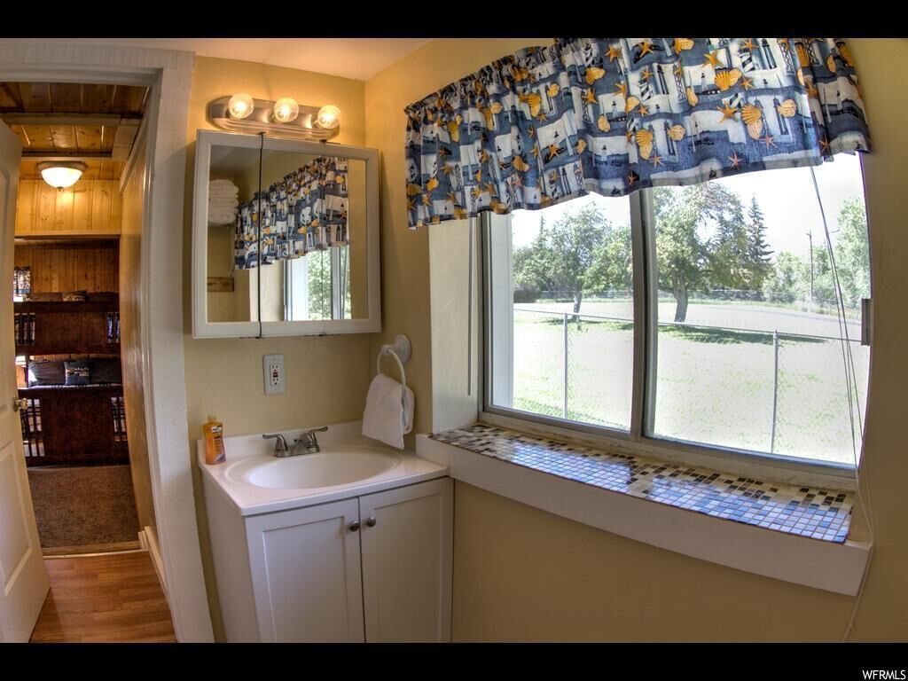 Une salle de bain avec un lavabo, un miroir et une fenêtre agrémentée d’une lambrequin à motifs.