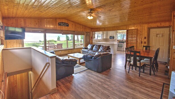A wooden cabin interior with a living area, dining table, and kitchen. - Lake-front Cabin Located In The Heart Of Bear Lake! (Garden City)
